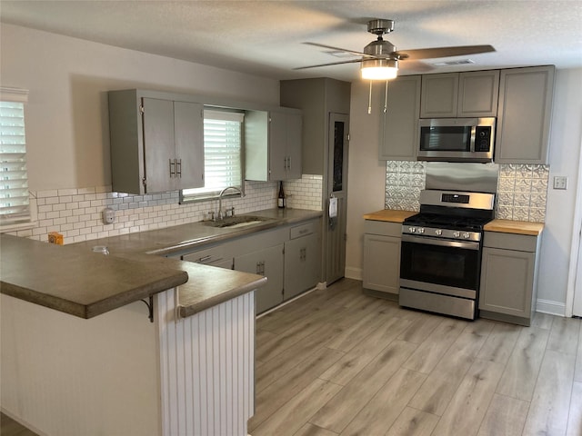 kitchen with stainless steel appliances, a peninsula, a sink, visible vents, and gray cabinets