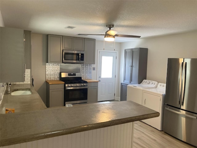 kitchen with appliances with stainless steel finishes, a peninsula, gray cabinetry, separate washer and dryer, and a sink