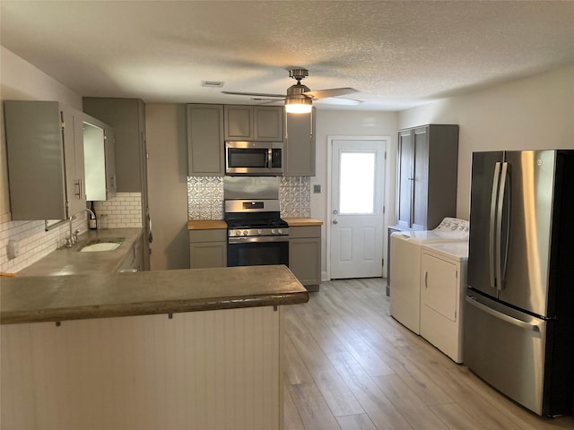 kitchen with light wood finished floors, gray cabinetry, appliances with stainless steel finishes, a sink, and independent washer and dryer