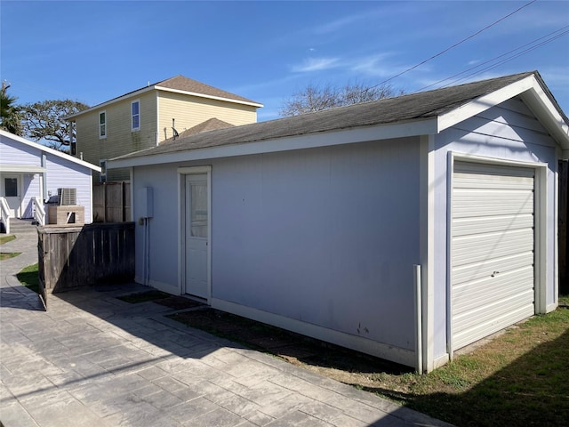 exterior space featuring a garage, an outbuilding, roof with shingles, and a patio