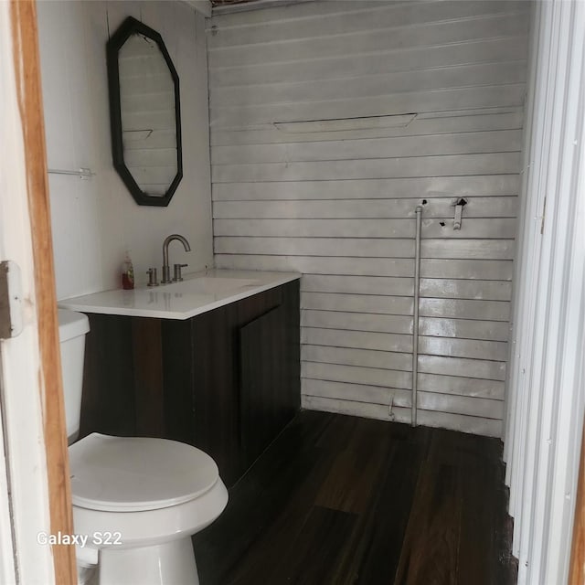 bathroom featuring wood finished floors, wood walls, vanity, and toilet