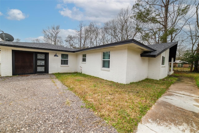 ranch-style home with brick siding, roof with shingles, gravel driveway, and a front lawn