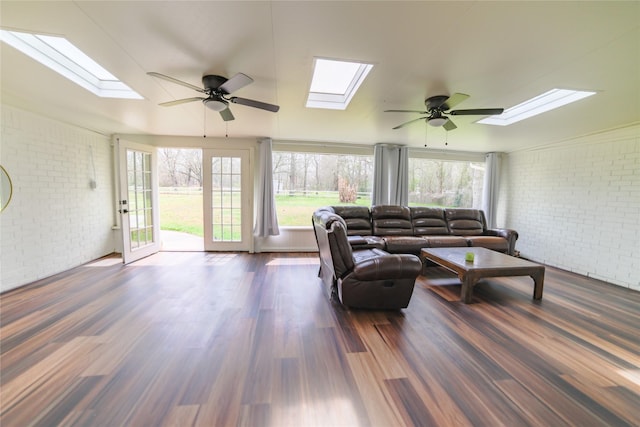 living area featuring ceiling fan, brick wall, a skylight, and dark wood finished floors