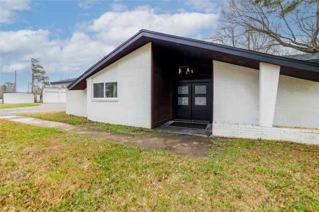 view of exterior entry featuring a yard, french doors, and brick siding