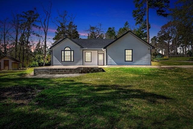 view of front of property with a shingled roof, a lawn, and an outdoor structure