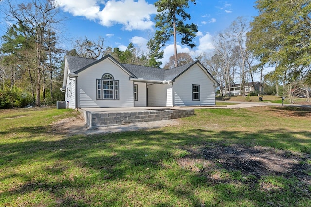 view of front facade with central AC unit, roof with shingles, and a front yard