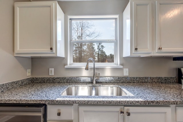 kitchen with stainless steel dishwasher, light stone counters, white cabinets, and a sink