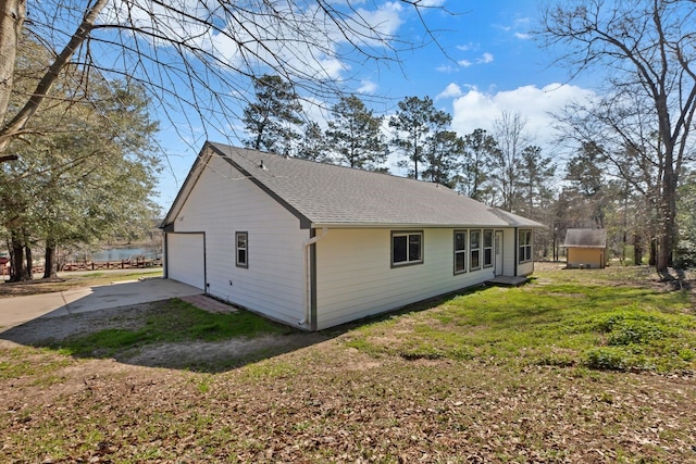 view of home's exterior with a shingled roof, a detached garage, a water view, concrete driveway, and a lawn