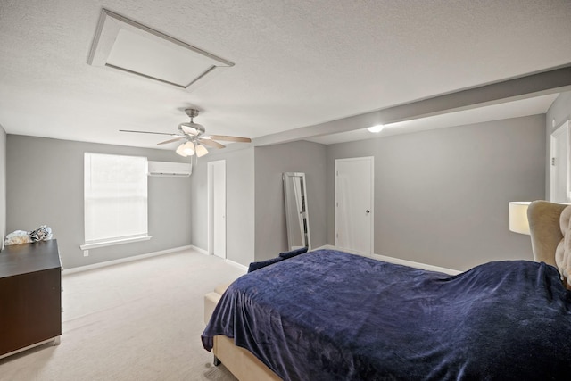 bedroom with ceiling fan, carpet, an AC wall unit, attic access, and a textured ceiling