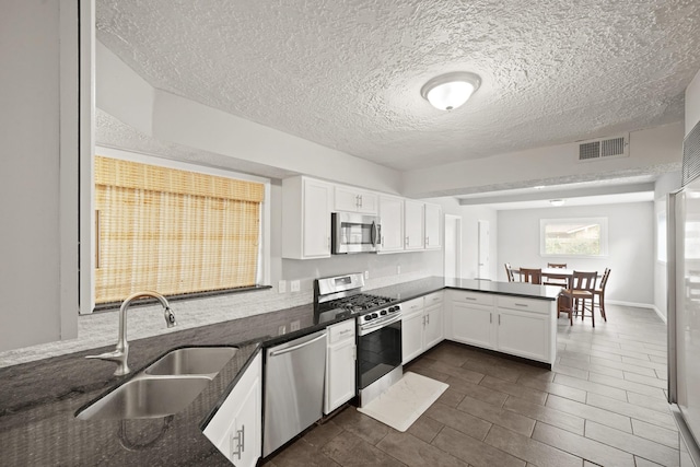 kitchen featuring visible vents, a peninsula, stainless steel appliances, white cabinetry, and a sink