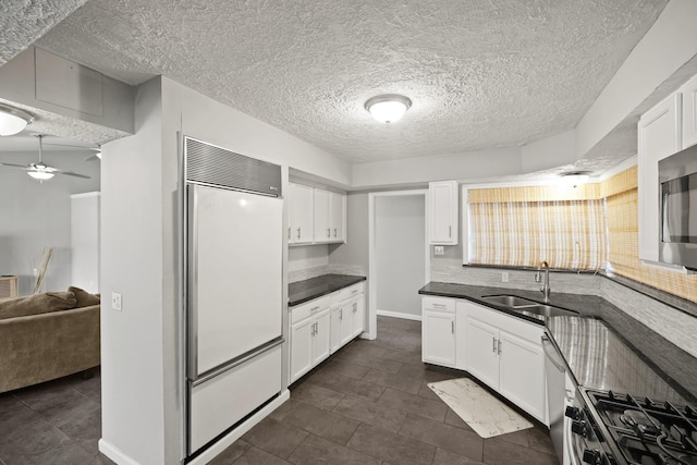 kitchen with a sink, dark countertops, appliances with stainless steel finishes, and white cabinetry