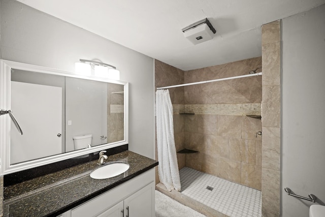 bathroom with toilet, tiled shower, and vanity