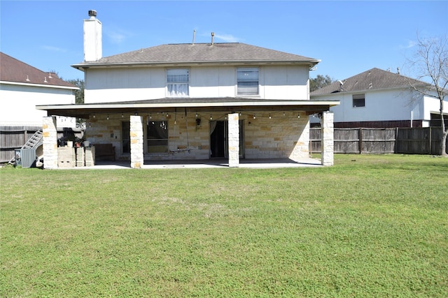 back of property with a patio area, a fenced backyard, stone siding, and a yard