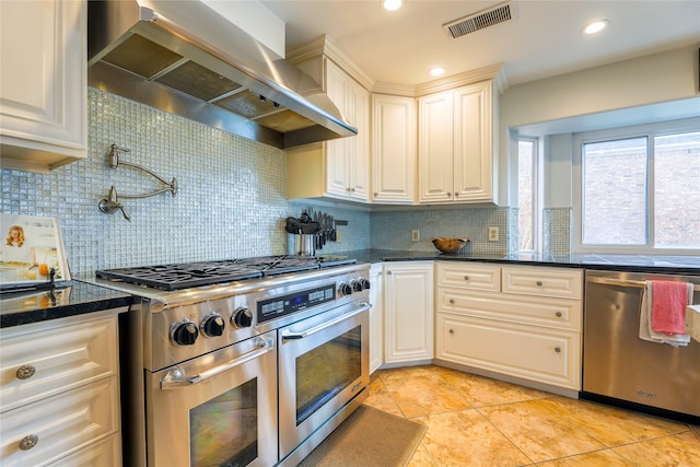 kitchen featuring visible vents, appliances with stainless steel finishes, wall chimney range hood, tasteful backsplash, and dark stone countertops