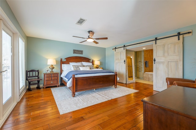 bedroom with a ceiling fan, hardwood / wood-style flooring, visible vents, and a barn door