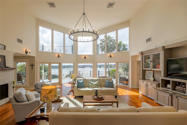 living area featuring light wood-style floors, a tile fireplace, visible vents, and a notable chandelier