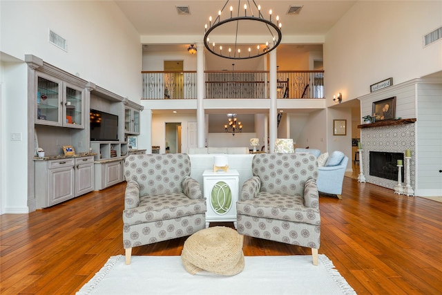 sitting room with a high ceiling, visible vents, a notable chandelier, and a glass covered fireplace