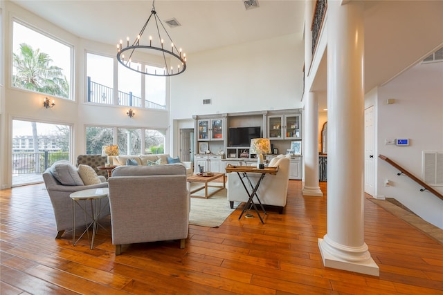 living room featuring a chandelier, a high ceiling, visible vents, wood-type flooring, and decorative columns