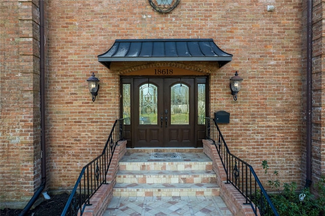 entrance to property featuring french doors, brick siding, metal roof, and a standing seam roof