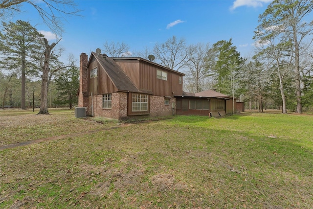 back of house with a lawn, central AC unit, brick siding, and a chimney