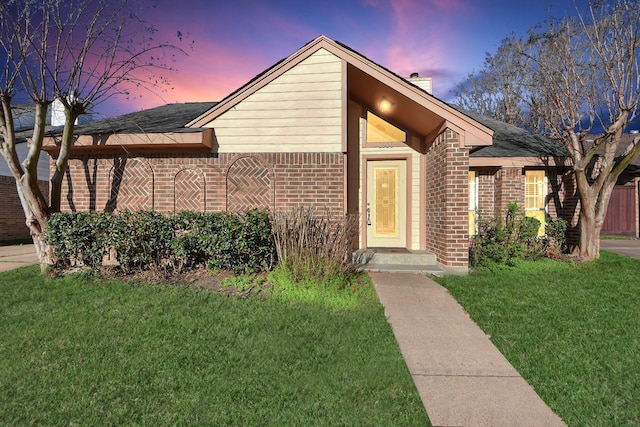 view of front of home with brick siding, a yard, and a chimney