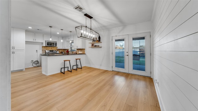 kitchen with dark countertops, stainless steel microwave, visible vents, light wood-style flooring, and white cabinets