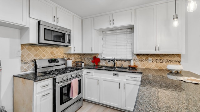 kitchen featuring appliances with stainless steel finishes, dark stone countertops, a sink, and white cabinets