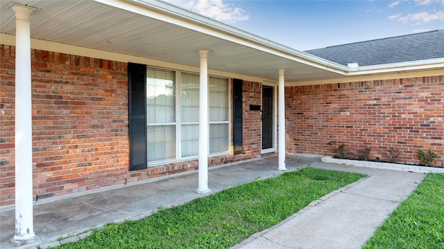 view of exterior entry featuring a shingled roof and brick siding