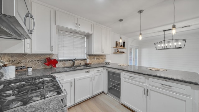 kitchen featuring stainless steel range with gas cooktop, white cabinets, a sink, beverage cooler, and a peninsula