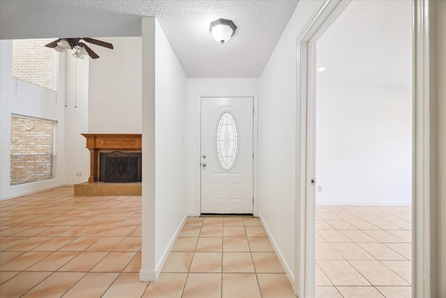 foyer with light tile patterned flooring, a fireplace with raised hearth, a textured ceiling, and a ceiling fan