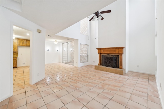 unfurnished living room featuring a fireplace with raised hearth, a ceiling fan, a high ceiling, light tile patterned floors, and baseboards