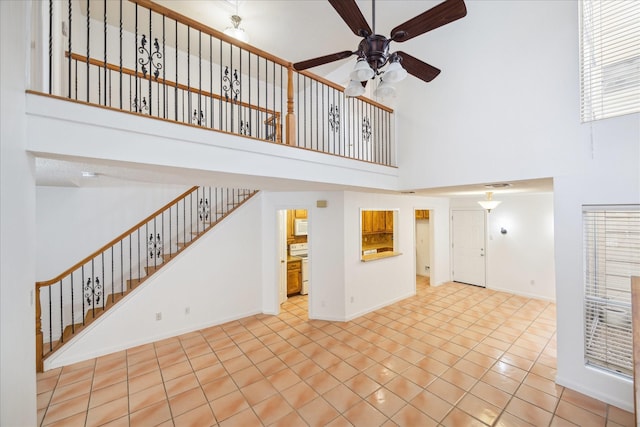 unfurnished living room with stairway, baseboards, a high ceiling, ceiling fan, and tile patterned floors