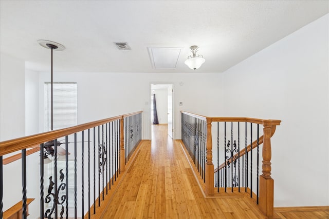 hall featuring visible vents, light wood finished floors, baseboards, attic access, and an upstairs landing