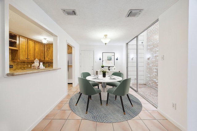 dining area featuring visible vents, a textured ceiling, light tile patterned flooring, and brick wall