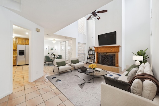 living room featuring light tile patterned floors, a fireplace with raised hearth, a high ceiling, and ceiling fan