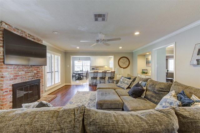 living room featuring dark wood-style floors, a fireplace, recessed lighting, visible vents, and ornamental molding