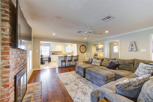 living room featuring recessed lighting, visible vents, a brick fireplace, dark wood finished floors, and crown molding