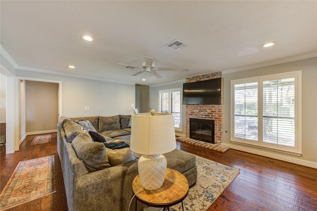 living area featuring a brick fireplace, dark wood-style floors, visible vents, and ornamental molding