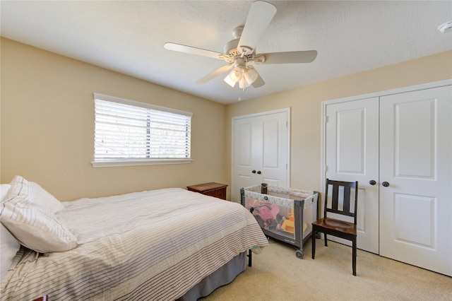 bedroom featuring light carpet, ceiling fan, and multiple closets