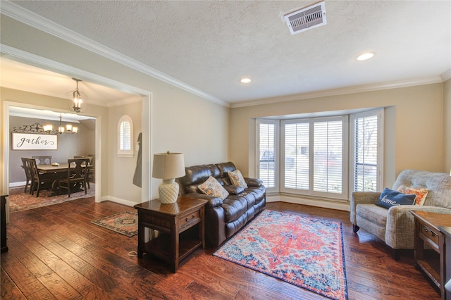 living room with a textured ceiling, hardwood / wood-style flooring, visible vents, an inviting chandelier, and crown molding