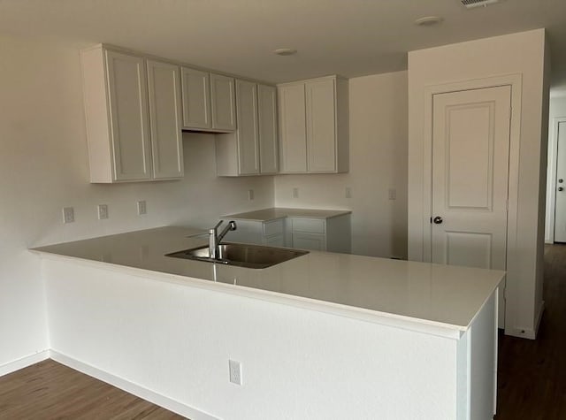 kitchen with baseboards, visible vents, dark wood-style floors, a peninsula, and a sink