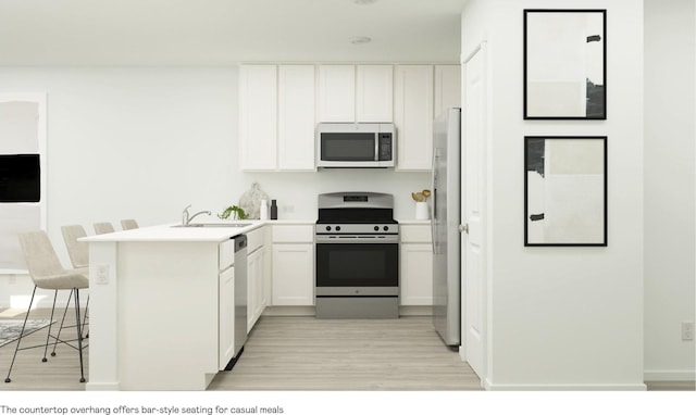 kitchen with a breakfast bar area, a peninsula, stainless steel appliances, white cabinetry, and a sink