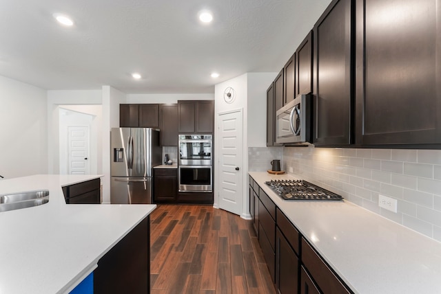 kitchen featuring a sink, light countertops, appliances with stainless steel finishes, decorative backsplash, and dark wood-style floors