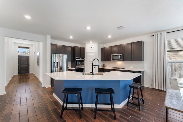 kitchen with a breakfast bar, stainless steel appliances, tasteful backsplash, a sink, and an island with sink