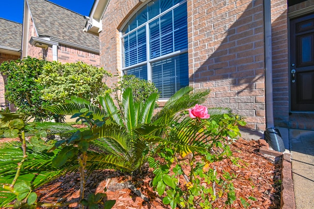 details featuring a downspout, gutters, brick siding, and roof with shingles