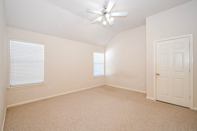 spare room featuring light carpet, ceiling fan, baseboards, and vaulted ceiling