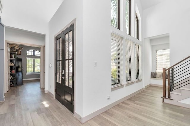 foyer entrance with stairs, baseboards, a towering ceiling, and light wood-style floors