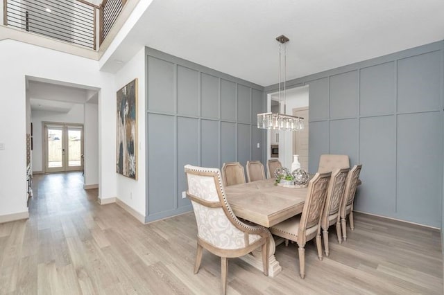 dining room featuring light wood-type flooring, an inviting chandelier, a decorative wall, and french doors