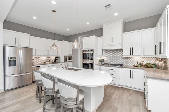 kitchen featuring a kitchen island with sink, stainless steel appliances, visible vents, white cabinetry, and light wood-type flooring