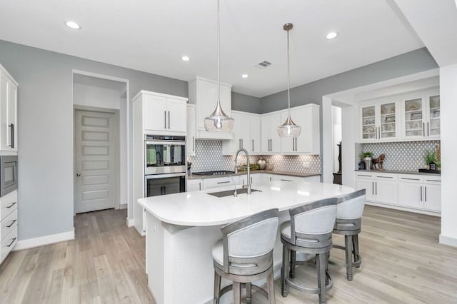 kitchen featuring light wood-style flooring, a kitchen breakfast bar, double oven, white cabinetry, and a sink